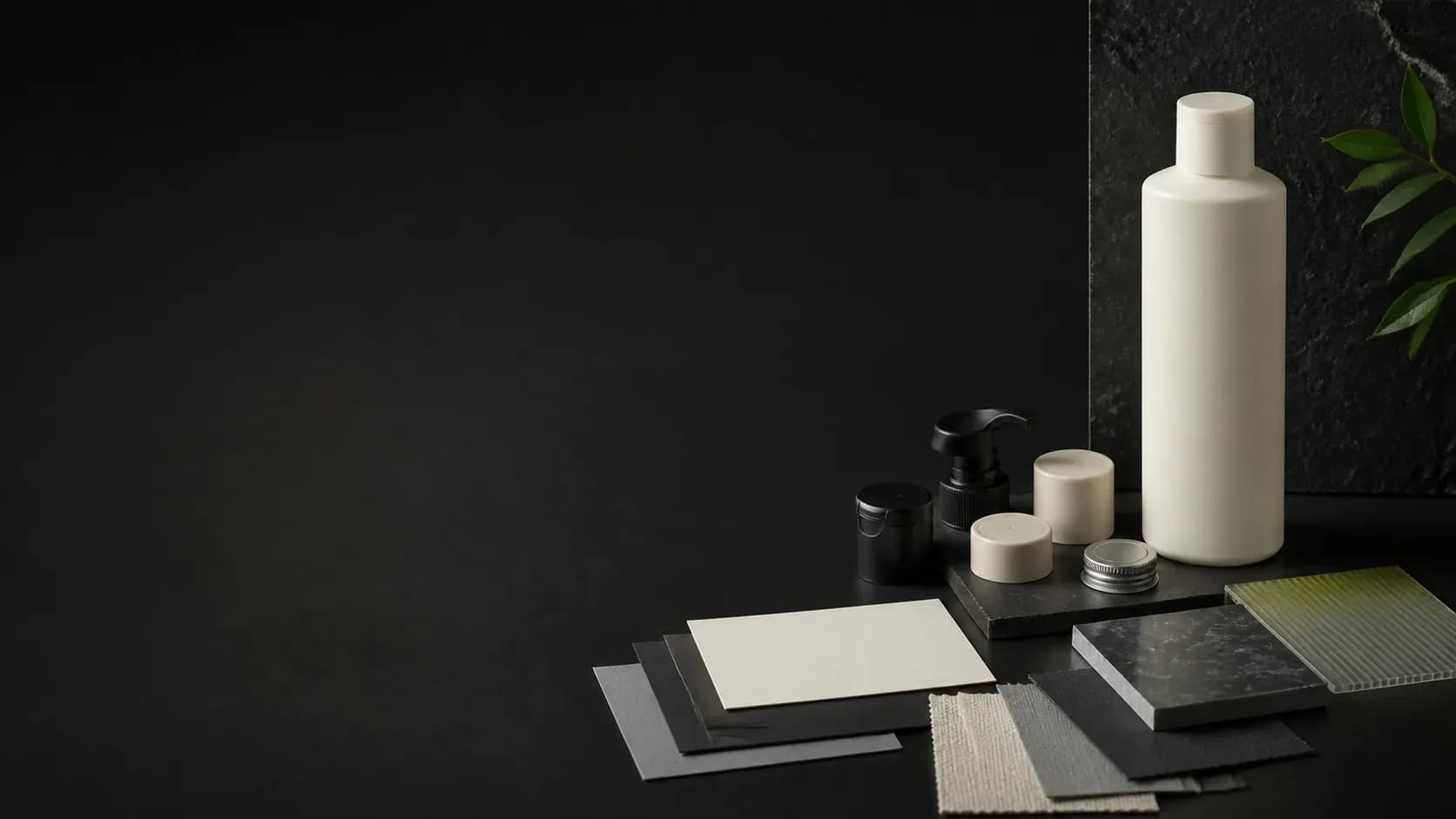 An unbranded haircare container, closure samples, material swatches, and blank brief cards on a dark project-planning table.